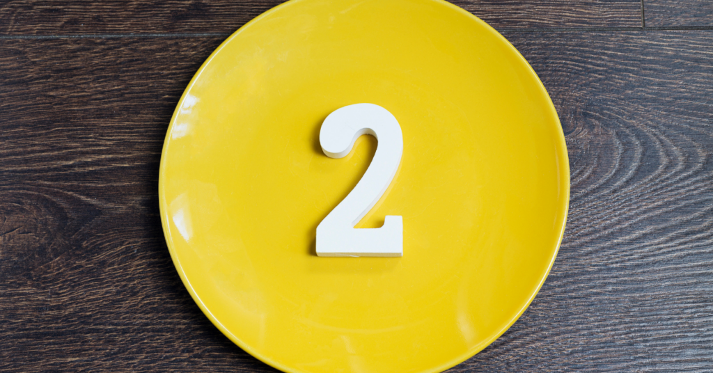 木目のテーブルに数字の2が乗っている黄色のお皿。
